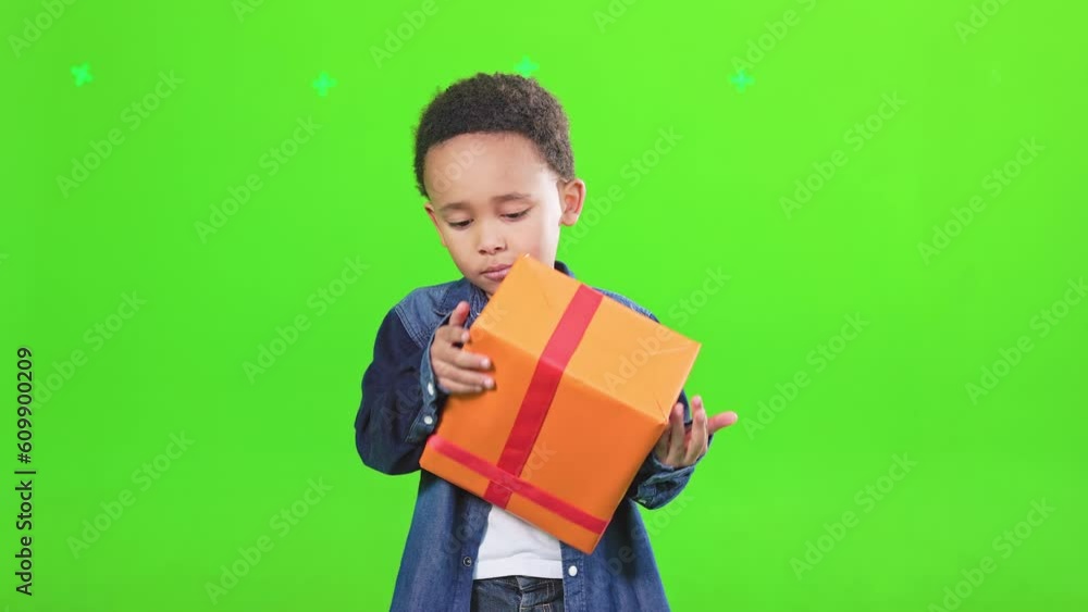 Curious little boy looking at big holiday gift box, guessing, what inside is, motion. Front view of african american male kid in shirt hugging wrapped present, isolated on green. Celebration concept. Curious little boy looking at big holiday gift box, guessing, what inside is, motion. Front view of african american male kid in shirt hugging wrapped present, isolated on green. Celebration concept.