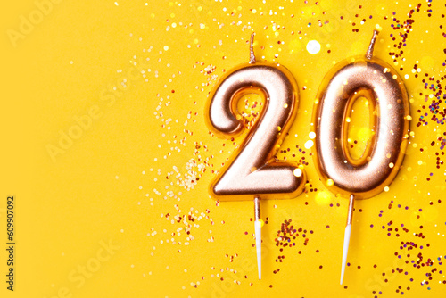 Gold candles in the form of number twenty on yellow background with confetti. 20 years anniversary celebration.