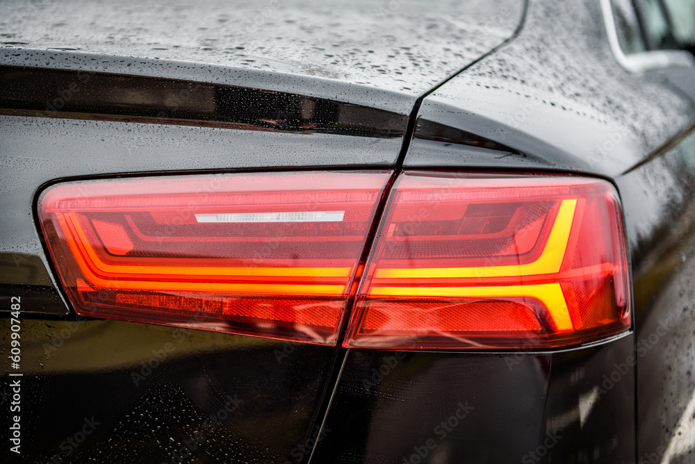 Car tail light. Detail black metallic car with rear light close up. Rear lamp signals for turning car on street. Right back modern headlight car. Signal function to keep them distance. Trunk closeup.