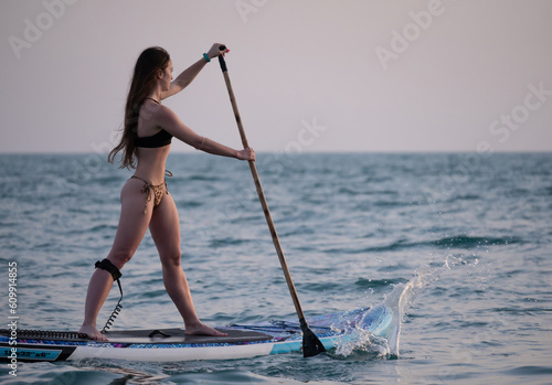 sexy girl on a sup board in the sea with a paddle professionally swims beautifully and gracefully