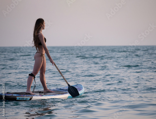 sexy girl on a sup board in the sea with a paddle professionally swims beautifully and gracefully