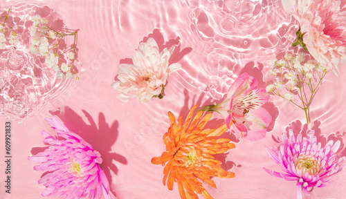 Summer creative layout with pink, orange flowers in pastel pink water ripple background. 80s or 90s retro aesthetic fashion cosmetic idea. Minimal summer idea.