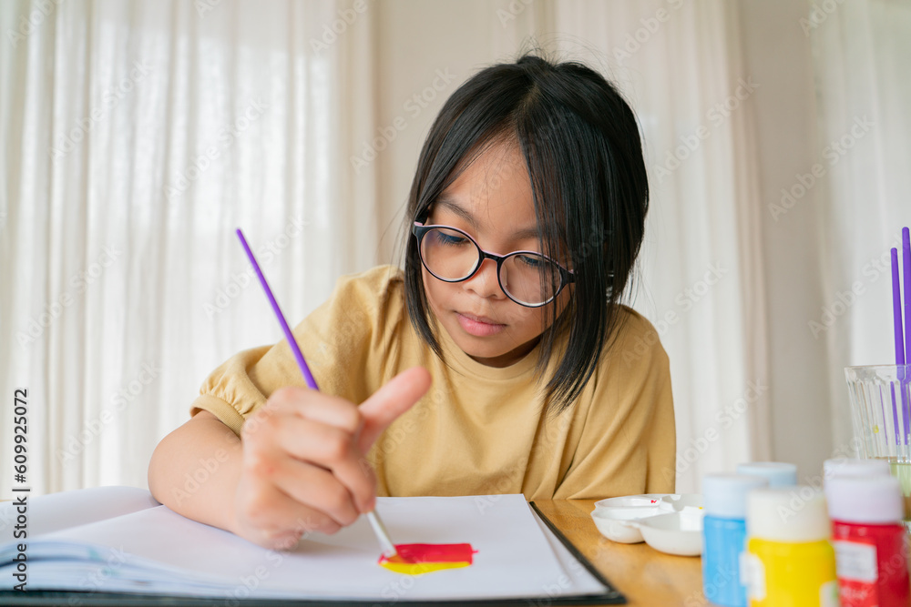 Young girl asian sitting and painting watercolour artwork to develop abilities and improve mental health at home. Female artist drawing with inspiration.