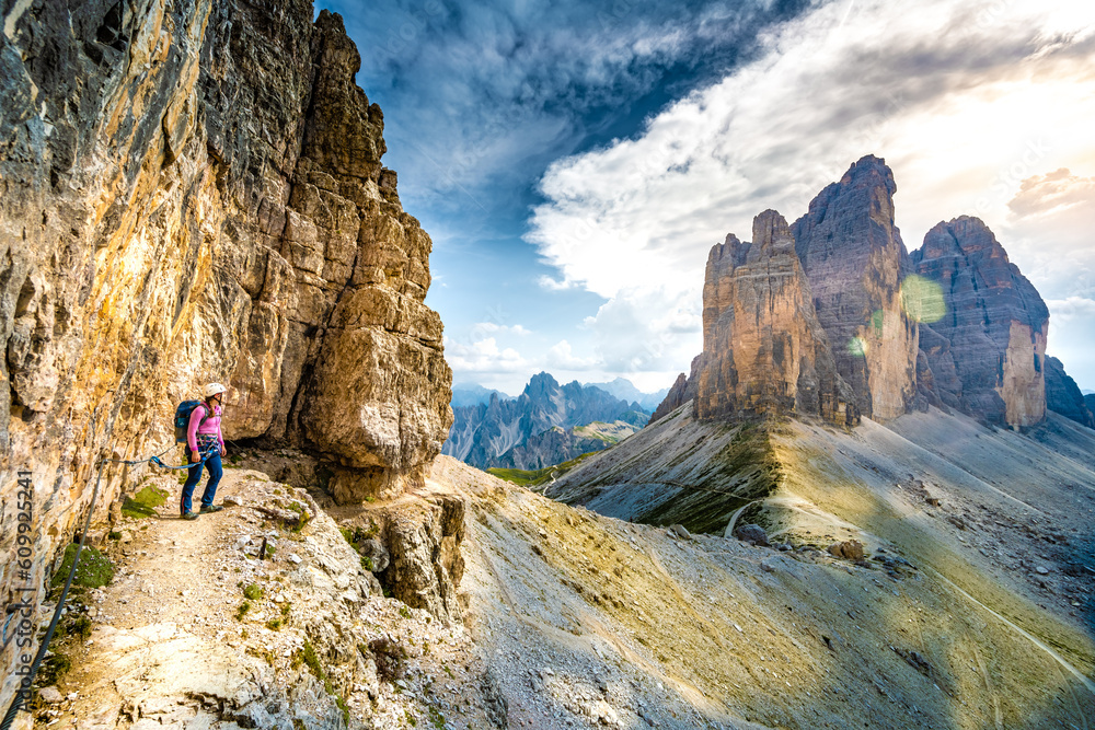 Young athletic woman enjoys scenic view on Tre Cime from via ferrata in the evening. Tre Cime, Dolomites, South Tirol, Italy, Europe.