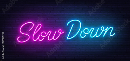 Slow Down neon lettering on brick wall background.