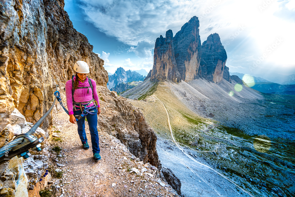 Young athletic woman walks on via ferrata trail with scenic view on Tre Cime in the evening. Tre Cime, Dolomites, South Tirol, Italy, Europe.