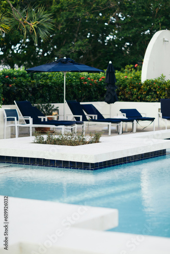 vacation and holiday concept, blue sunbeds and outdoor chairs near umbrellas around green palm trees and tropical plants next to outdoor swimming pool in hotel, luxury resort, summer