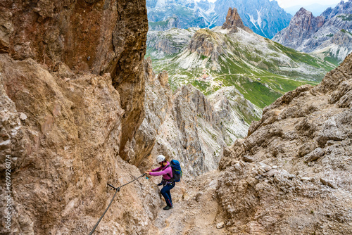 Young athletic woman hikes in via ferrata in the evening. Tre Cime, Dolomites, South Tirol, Italy, Europe.