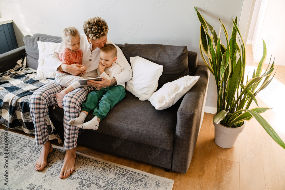 Father and his kids watching cartoons on digital tablet while sitting on couch Father and his kids watching cartoons on digital tablet while sitting on couch