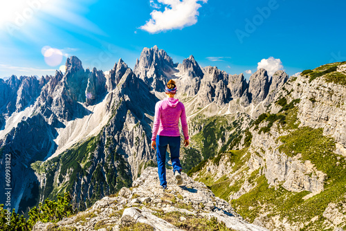 Athletic woman walks on epic view point with Cadini di Misurina mountain range in the morning. Tre Cime, Dolomites, South Tirol, Italy, Europe.