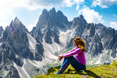 Sitting woman enjoys epic view on Cadini di Misurina mountain range in the morning. Tre Cime, Dolomites, South Tirol, Italy, Europe.