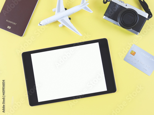flat lay of digital tablet with blank white screen, airplane model, passport, credit card and digital camera isolated on yellow background. travel planning concept.