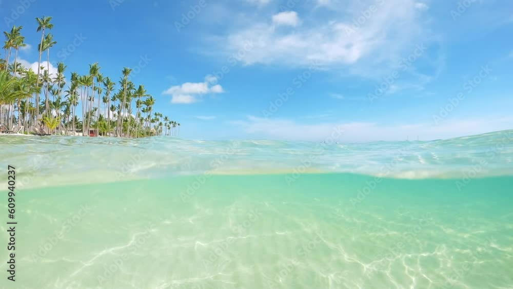 Half underwater slow motion turquoise sea water at the exotic sandy beach on the tropical Island. Idyllic view of ocean and the white sand coast with palm trees in all-inclusive resort Half underwater slow motion turquoise sea water at the exotic sandy beach on the tropical Island. Idyllic view of ocean and the white sand coast with palm trees in all-inclusive resort