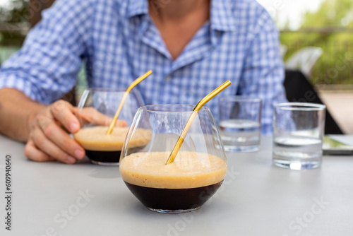 A man drinking Caffe shakerato with a metal straw. Italian cold drink prepared using espresso and ice cubes in a cocktail shaker. Italian summer coffee beverage. Italy. photo