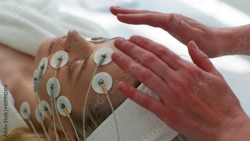 Close-up top rear view of pretty young woman patient preparing for myostimulation procedure in modern beauty clinic. Physiotherapist putting electrodes of myostimulator during bioresonance therapy. photo