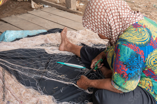 Cambogia,donna anziana aggiusta una rete da pescatore