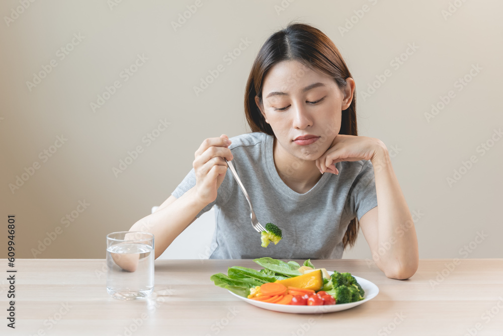 unhappy asian women is on dieting time looking at broccoli on the fork. girl do not want to eat vegetables and dislike taste unhappy asian women is on dieting time looking at broccoli on the fork. girl do not want to eat vegetables and dislike taste