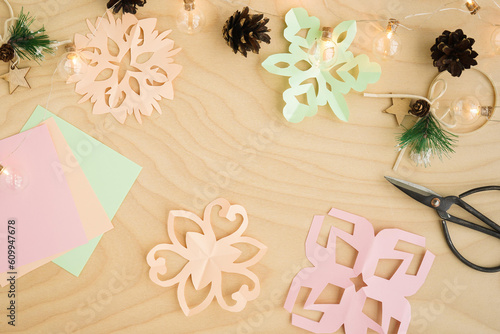 Colorful paper snowflakes cutouts, on a wooden background. Cutting snowflakes from colored paper. Snowflake winter background. Simple winter kids crafts idea. Copy space