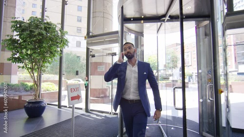 Attractive Indian business man in a smart suit walks through the lobby of a building on his phone, in slow motion