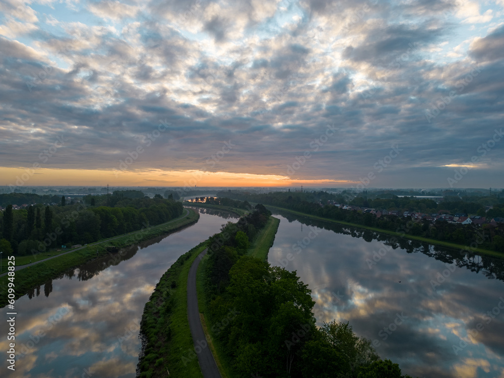 Sunrise or sunset over the river and beautiful morning or evening landscape of Duffel, Antwerp, Belgium. Evening sun breaks through the clouds and the trees. Flight over calm river with reflection