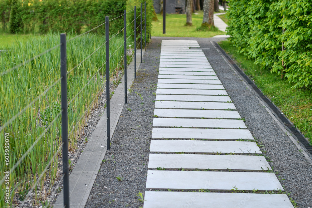 Paved stone walkway in the garden surrounded by lawn and wild grass. 