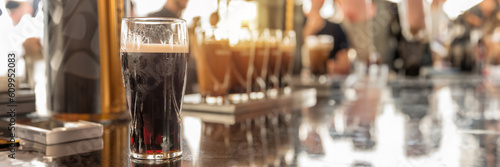 Glasses of stout beer on a bar counter, blurred people, panoramic pub header