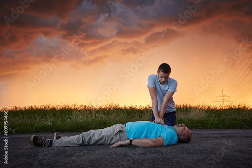Dramatic resuscitation on rural road. Young man provides first aid to unconscious middle aged man under storm clouds. Themes rescue, help and hope.. photo