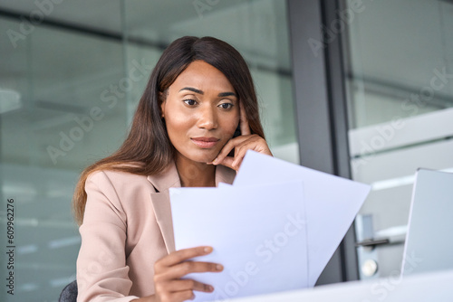 Busy young African American business woman account manager executive expert checking tax papers, analyzing corporate bills thinking on risks reading corporate financial report working in office.