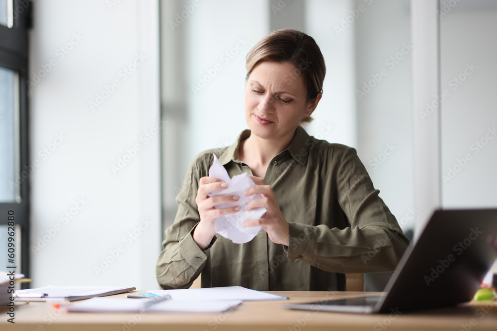 Woman in khaki blouse crumples paper at table in office Woman in khaki blouse crumples paper at table in office