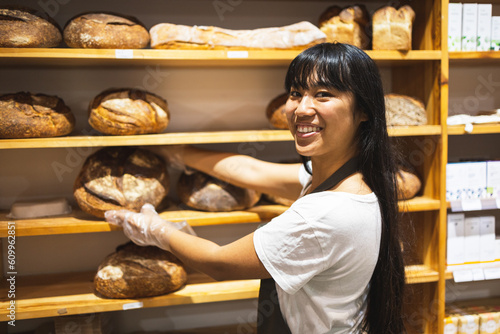 Happy Asian woman with bread loaves in bakery