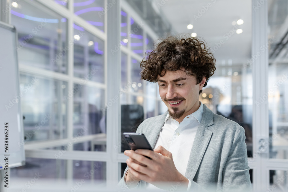 Successful and happy businessman with beard works in modern bright office, male boss uses laptop, business owner in casual shirt holds phone, browses internet pages. Successful and happy businessman with beard works in modern bright office, male boss uses laptop, business owner in casual shirt holds phone, browses internet pages.