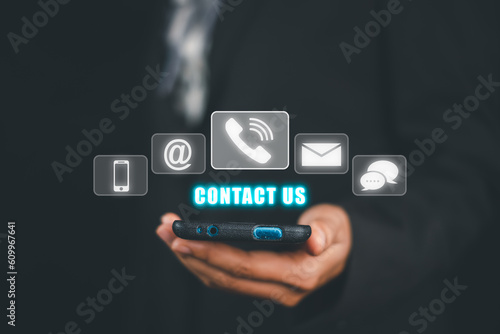 Contact us or Customer support hotline people connect, Person hand using smart phone with Contact us icon on VR screen on office desk, email, address, live chat, internet wifi.