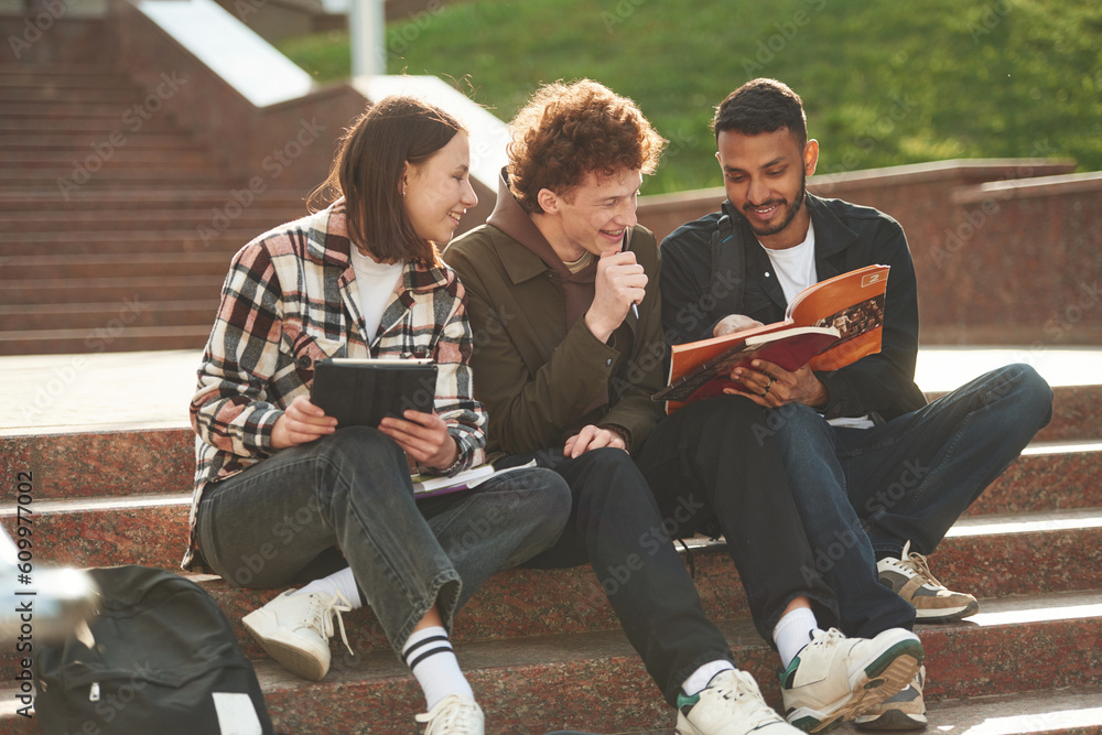 Fototapeta premium Students are sitting on the stairs. Young people in casual clothes are together outdoors