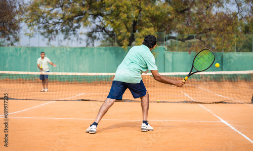 back view shot of indian senior man busy playing tennis by hitting ball with racquet at court - concept of mistakes, practising and learning © WESTOCK