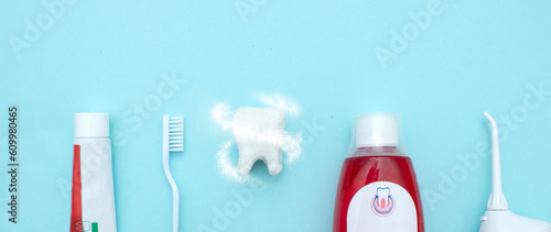 Close up of a toothbrush, toothpaste, irrigator, mouthwash for teeth, dental mirror with white molar tooth model and Protective vortex around tooth on blurred blue background. Oral Care Concept. 
