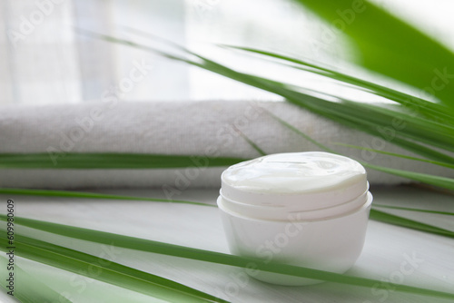 white cosmetic cream on a white wooden background surrounded by long green leaves