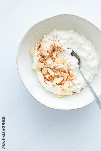 Cottage cheese with cinnamon and almonds in white bowl, white background. Healthy protein breakfast concept.