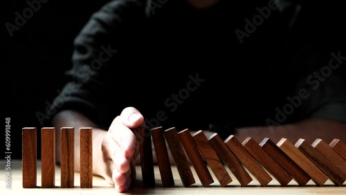 Close-up Businessman hand stopping domino effect, business crisis, risk protection on dark background. Concept of Risk, Management, Assessment, Business, Crisis, Financial, Planning, Economic photo