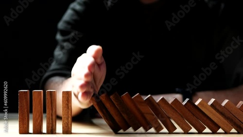 Close up Businessman hand stopping wooden domino business crisis effect or risk protection on dark background. Concept of Risk, Management, Assessment, Business, Crisis, Financial, Planning, Economic