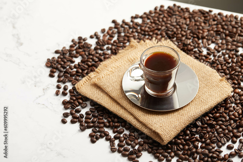 Cup of espresso coffee and coffee beans, on brown napkin, on white marble table