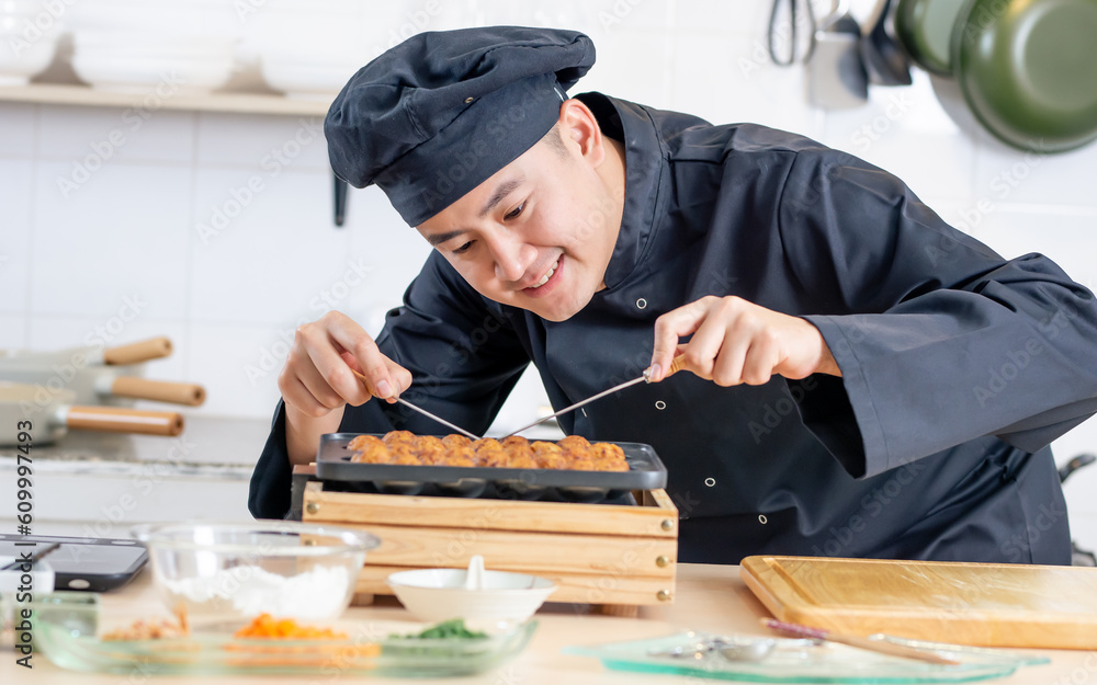 Portrait handsome professional Japanese male chef wearing black uniform, hat, cooking, making takoyaki street food, smiling with confidence, standing in kitchen. Restaurant, Hotel Concept. Portrait handsome professional Japanese male chef wearing black uniform, hat, cooking, making takoyaki street food, smiling with confidence, standing in kitchen. Restaurant, Hotel Concept.