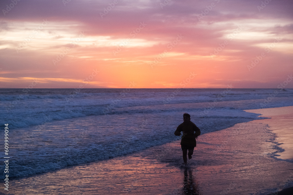 Silueta de niño corriendo en la playa durante el atardecer