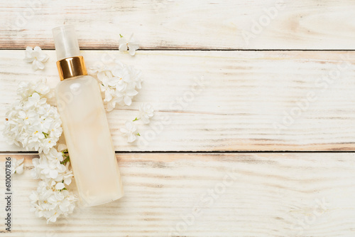 Composition with cosmetic bottle and flowers on wooden background, top view