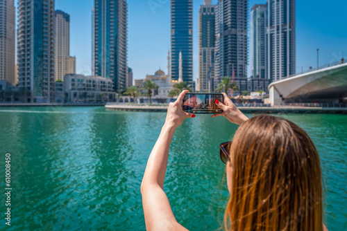 Canvas Print A young woman takes a photo with her mobile phone on the Dubai Marina Promenade