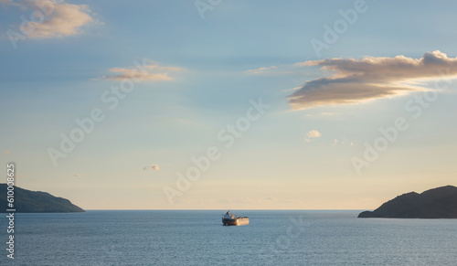 view of container cargo ship or Fishing trawler sailing over calm sea , towards next commercial port, travel in Turkey, Fethiye city. sunset time over Calish beach