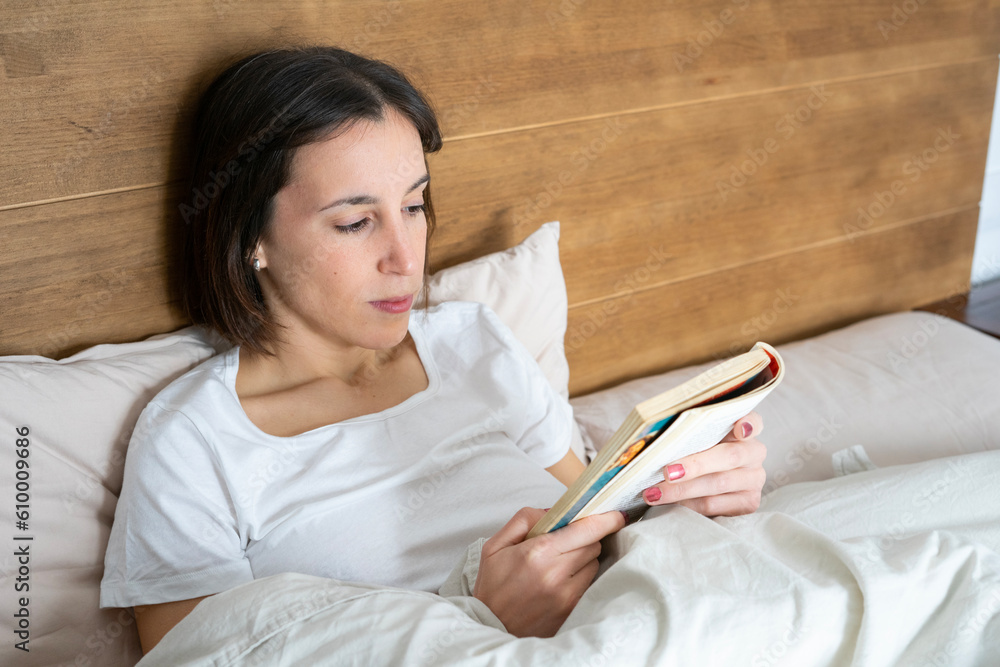 girl stretched out in bed reading a book girl stretched out in bed reading a book