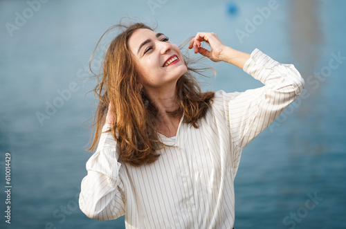 Portrait of beautiful woman against sea background. Girl wearing casual clothes. Young woman smiling and looking up at sky. Walking by sea on sunny day. Happy young woman on holiday.