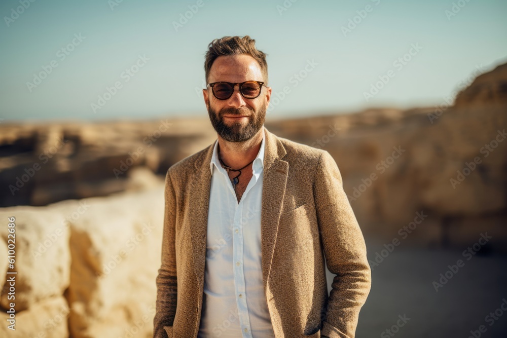 Portrait of a handsome bearded man wearing sunglasses and a coat standing in a desert Portrait of a handsome bearded man wearing sunglasses and a coat standing in a desert