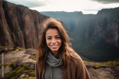 Happy young woman standing on the edge of a cliff and looking at the camera