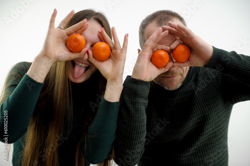 A young couple holds Mandarins instead of eyes like glasses. Cheerful couple. Lovers fooling around. High quality photo